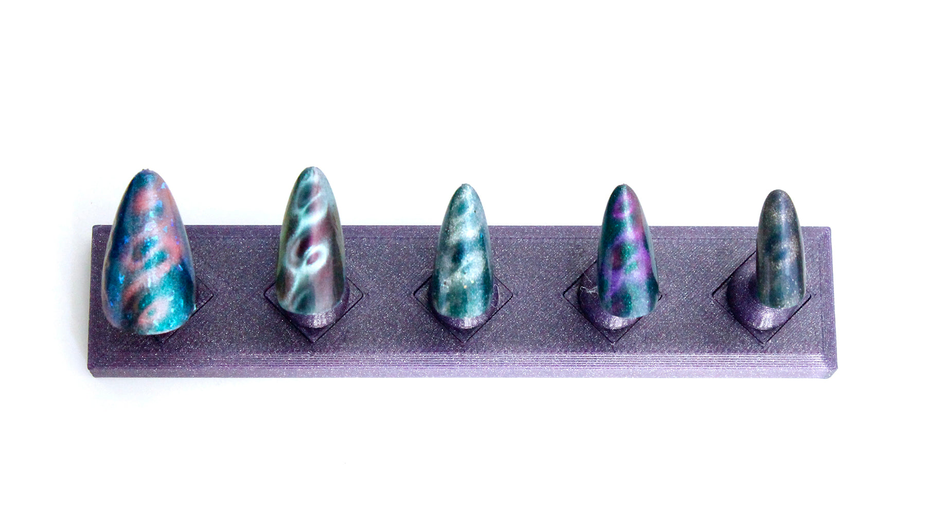 Five colorful nail tips on a gray stand against a white background