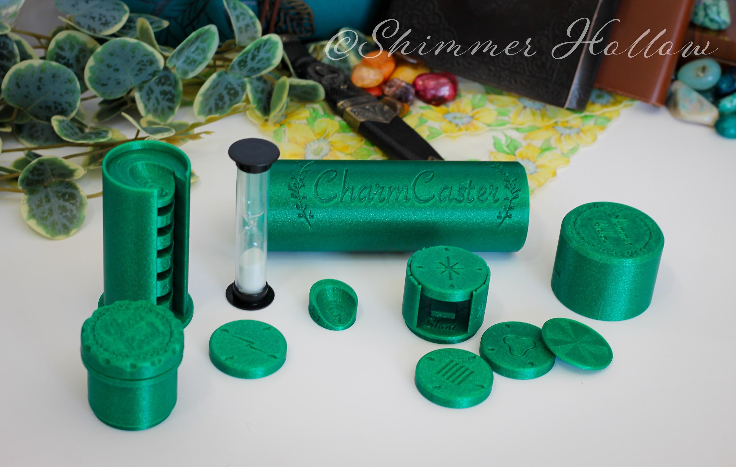 Green 3d printed product with 'CharmCaster' branding on a white surface. Includes design discs, glass bead spinning attachment, a sand hourglass timer, and finger podiums of varying sizes.